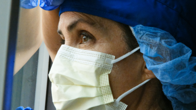 Health care worker wearing mask and looking out a window