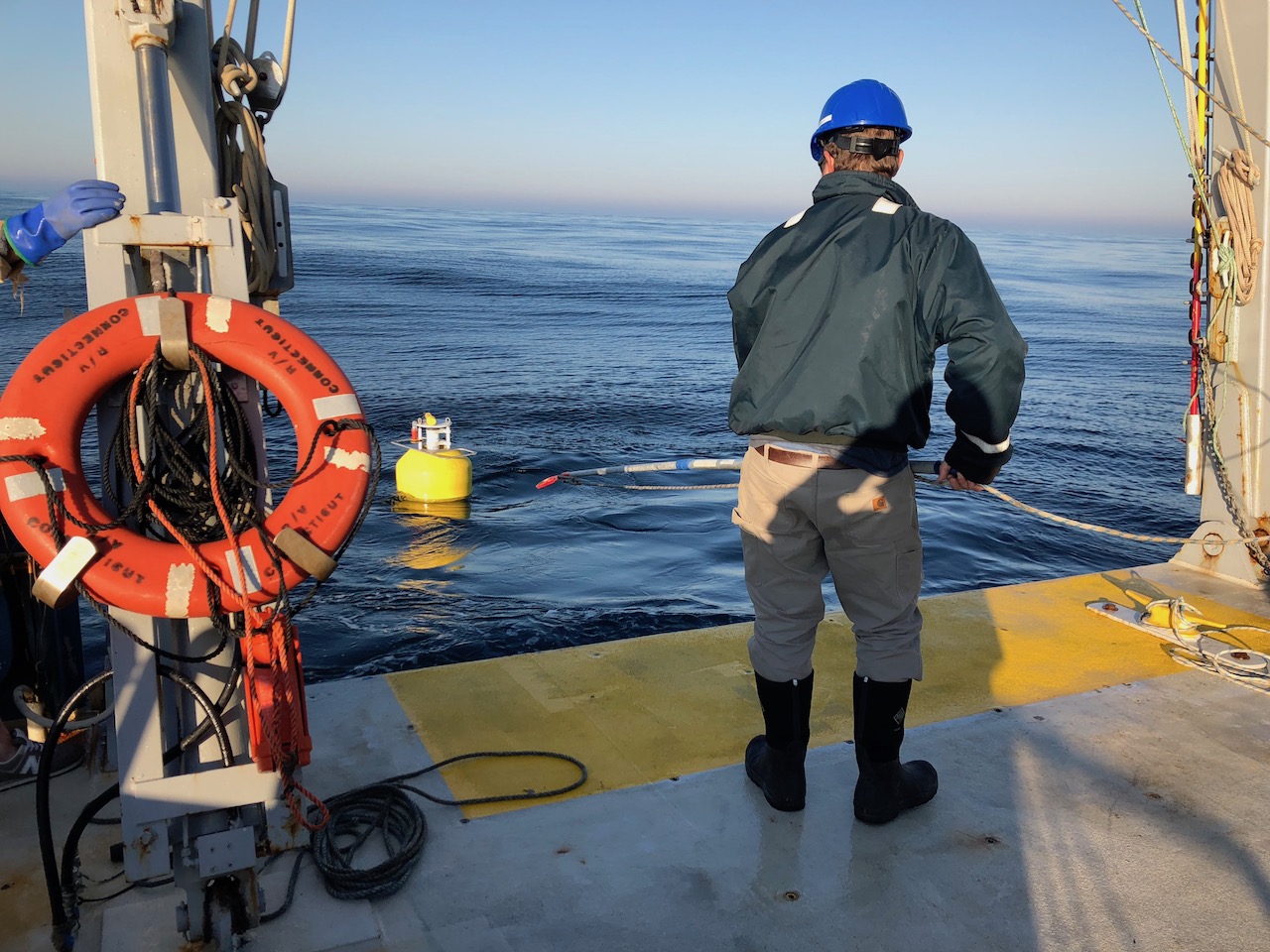 biologist wearing hard hat lowering gear into the water from the stern of a boat