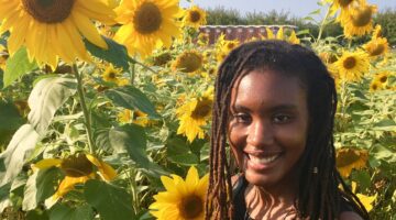 Black woman with dreadlocks standing in a field of sunflowers