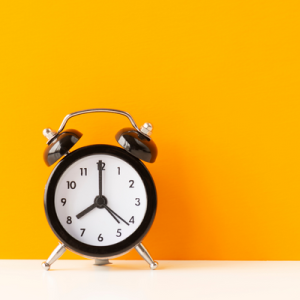 manual alarm clock (black with white face) against bright orange backdrop